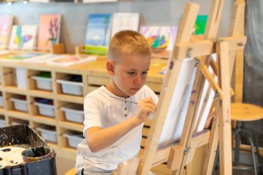 Sarışın bir çocuk resim dersinde sehpaya resim çizer. Çocukların yaratıcılığı kavramı..