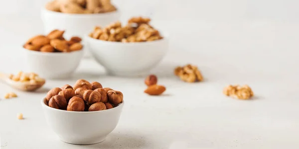 Hazelnuts and other nuts in white bowls on a white background. Banner — Stock fotografie