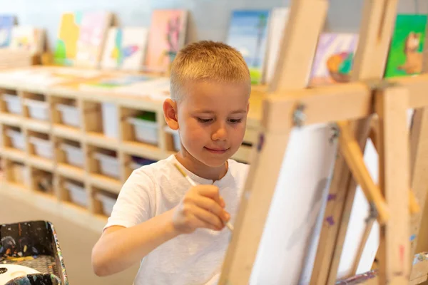 Sonriente chico rubio dibuja sobre lienzo en el taller. Clases de dibujo para niños —  Fotos de Stock