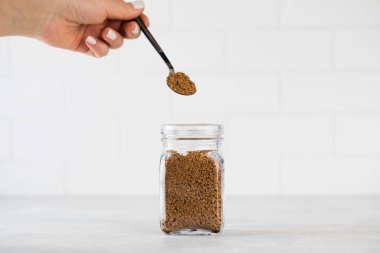 Bir kadının eli, küçük bir kaşıkla hazır kahveyi kahve kavanozunun üzerinde tutar..