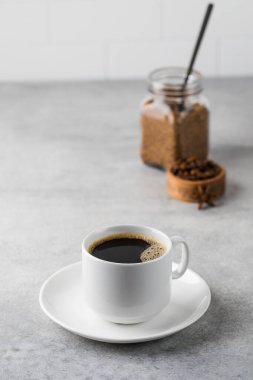 Beyaz bardakta sade kahve, gri bir masanın üstünde çay tabağı. Boşluğu kopyala.