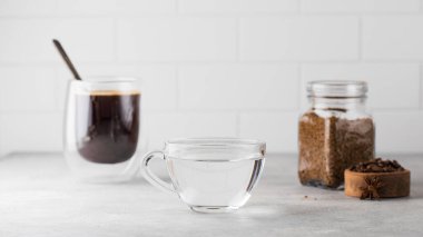 Gri masada bir kupa su, bir kupa sade kahve ve bir kavanoz hazır kahve var..