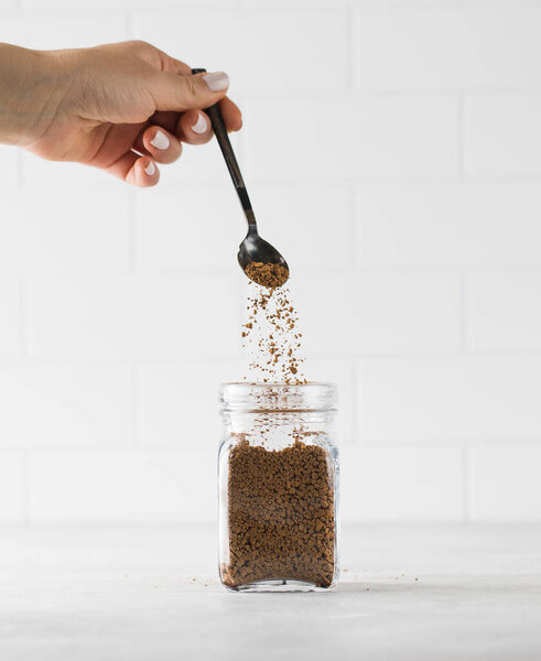Женская рука наливает растворимый кофе в стеклянную банку.