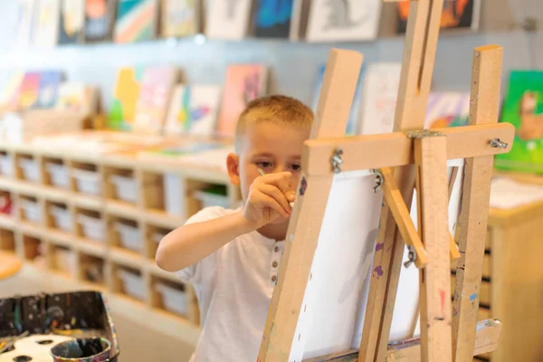 Un chico rubio dibuja en un caballete en una lección de dibujo. El concepto de creatividad infantil. —  Fotos de Stock