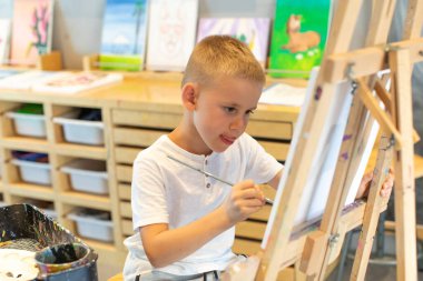 Sarışın bir çocuk resim dersinde sehpaya resim çizer. Çocukların yaratıcılığı kavramı..