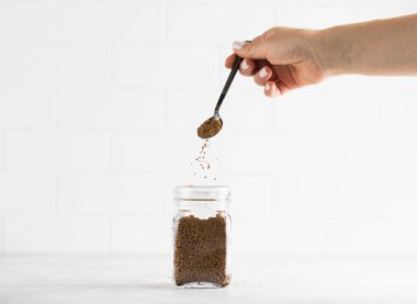 Bir kadının eli cam kavanoza hazır kahve koyar..