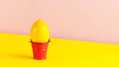 Renkli bir arka planda dekoratif kovada sarı Paskalya yumurtası. Paskalya konsepti. Boşluğu kopyala.