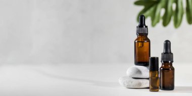 Açık gri arkaplanda taşlardan yapılmış bir kaidede kozmetik ürünleri olan cam damlalar. Boşluğu kopyala.