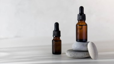 Kahverengi cam şişeler, taşların üzerinde deri yağı ve gölgeli açık arkaplan. Boşluğu kopyala.