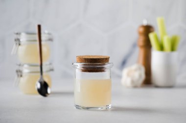 Cam saklama kavanozlarında kemik suyu çorbası, arka planda baharat ve kereviz. Sağlıklı beslenme kavramı.