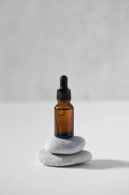 Kahverengi bir cam damlatıcı açık gri arka planda yüzün derisi için serumla taşların üzerinde durur. Bakım kozmetikleri.