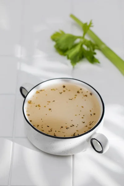 Kaldu tulang yang sehat dengan rempah-rempah dalam mangkuk di atas ubin putih dengan pola bayangan. — Stok Foto