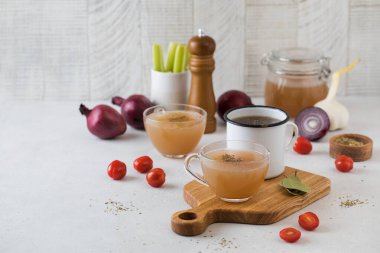 Ev yapımı kemik suyu, ahşap bir sopa üzerinde baharat, domates ve soğan bulunan kupalarda. Boşluğu kopyala.