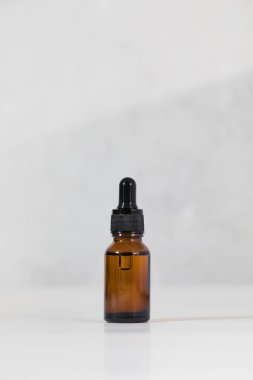 Açık gri arka planda yüz derisi için serumu olan kahverengi cam damlası. Bakım kozmetikleri.