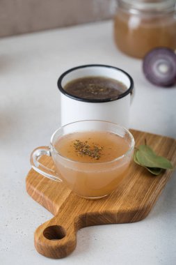 Ev yapımı kemik suyu bardakta, ahşap sopada baharat ve defne yaprağı..