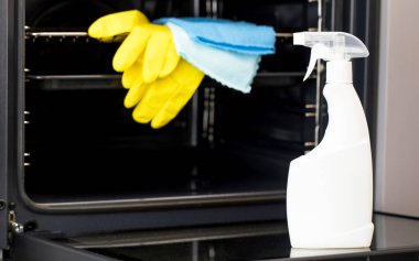 Açık bir fırının kapısında beyaz bir sprey şişesi ve fırın deterjanı var. Mutfağın genel temizliği.