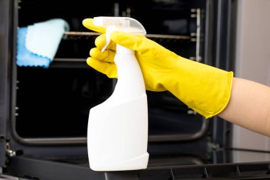  Temizlikçi fırının önünde sarı bir eldivenle bir deterjan şişesi tutuyor.. 