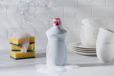 Köpüklü bulaşık jeli, gölgeli sabun köpüğü ve sarı süngerli beyaz plastik. 