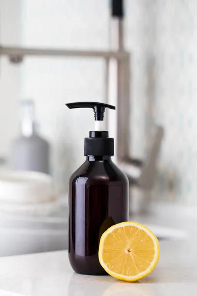 Botol dengan ramah lingkungan deterjen cuci piring dengan lemon di latar belakang wastafel dengan piring kotor. — Stok Foto
