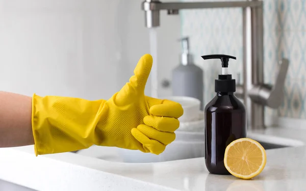Una botella de detergente lavavajillas ecológico con limón y una mano con guantes amarillos que muestra los pulgares hacia arriba. — Foto de Stock