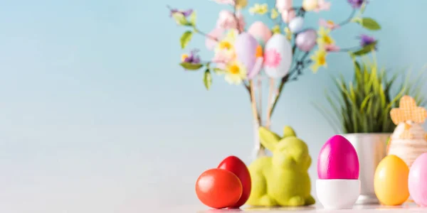 Easter banner with colorful eggs and a green rabbit on a blue background with a flower branch. Copy space — Stock Photo, Image