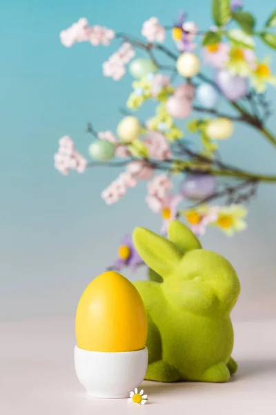 Easter card with a painted egg and a decorative figure of a hare on a blue background with flowers. — Stock Photo, Image