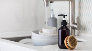 Çevre dostu bulaşık deterjanı ve lavabonun arka planında fırça olan bir şişe..