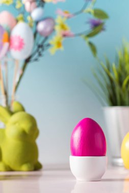 Boyanmış yumurtalı Paskalya kartı ve mavi arka planda çiçekli dekoratif bir tavşan figürü.. 