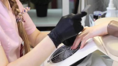 Bir manikürcü metal bir dosyayla çivi çakıyor. Güzellik salonunda manikür işlemi.