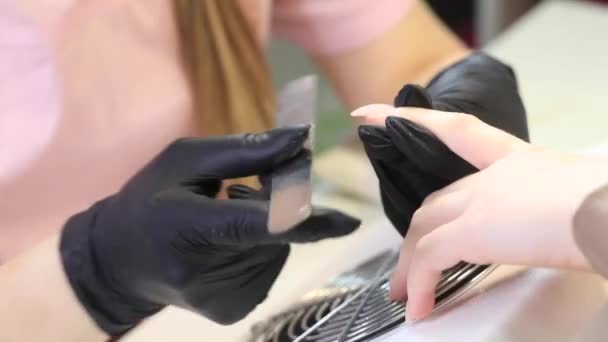 Manikűrös eltávolítja a sellak a körmök egy fém fájlt. A manikűr folyamata — Stock videók