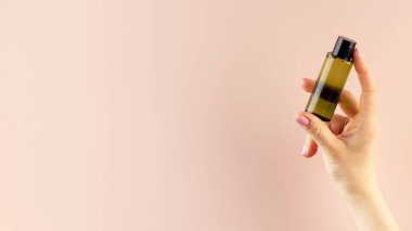 Kadının elinde pembe arka planda kozmetik ürünü olan bir şişenin maketi. Tuvalet malzemeleri kavramı.