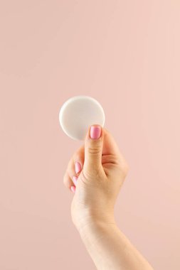 Bir kadının eli açık pembe arka planda yuvarlak bir sabunu tutar..