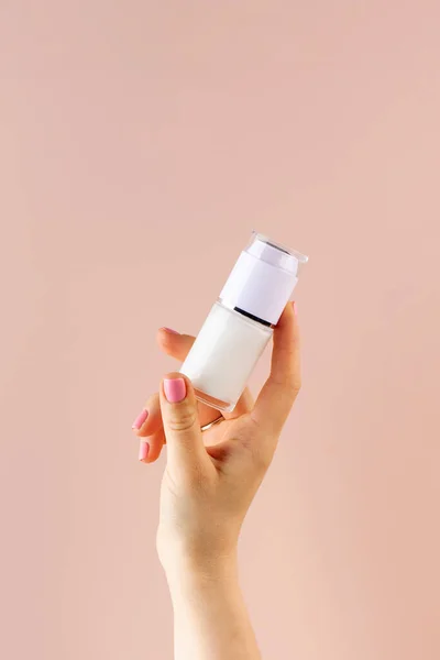 A mock-up of a jar of moisturizer in a womans hand on a pink background.