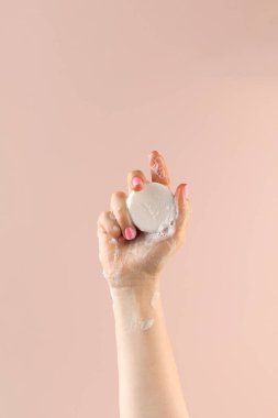 Bir kadının eli açık pembe arka planda yuvarlak bir sabunu tutar..