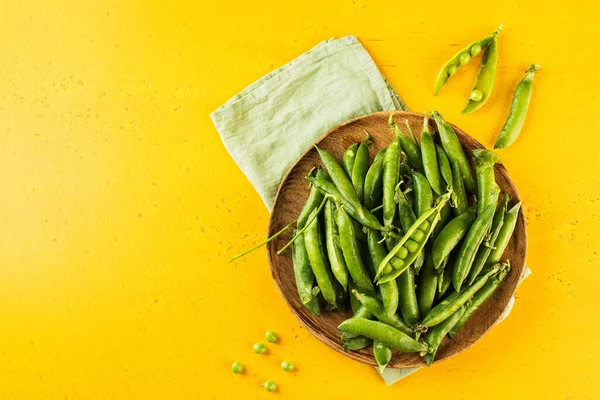 Guisantes verdes jóvenes maduros en un plato de madera sobre un fondo amarillo. Copiar espacio. —  Fotos de Stock