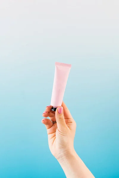 Mockup of a pink tube with a cosmetic product in a female hand on a blue background. Beauty product concept.