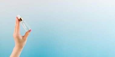  Mavi arka planda kadın elinin nemlendirici yağıyla cam damlatıcının bir kopyası. Boşluğu kopyala.