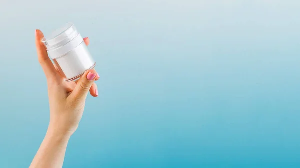 A mock-up of a jar of moisturizer in a womans hand on a blue background. Copy space.