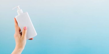 Mavi arka planda bir kadının elinde kozmetik ürünü olan beyaz bir dağıtıcının maketi..