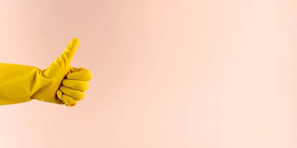 A hand in a yellow rubber glove for washing and cleaning shows a thumbs up. Copy space. Banner