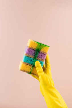 Sarı lastik eldivenli bir el, bulaşıklar için renkli süngerler tutar. Bulaşıklar için yeşil jel akar..