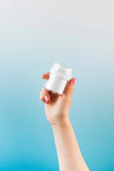 A mock-up of a jar of moisturizer in a womans hand on a blue background.