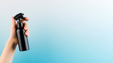 Mavi arka planda bir kadının elinde kahverengi pulvilizer ile profesyonel bir saç ürünü. Boşluğu kopyala. 