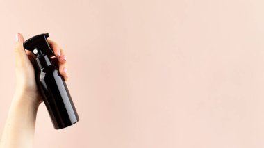 Pembe arka planda bir kadının elinde kahverengi pulvilizer ile profesyonel bir saç ürünü. Boşluğu kopyala. 