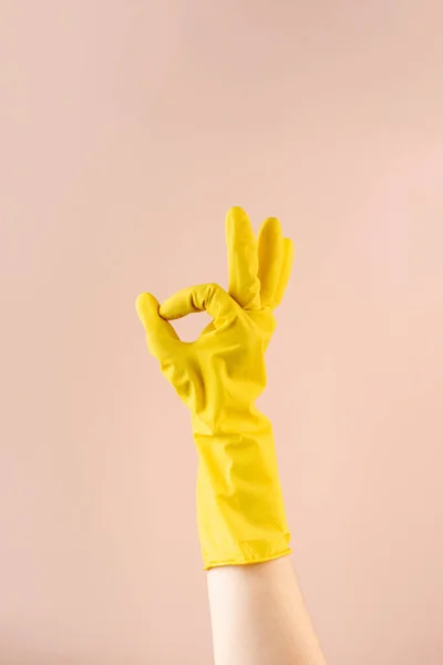 Hand in yellow rubber glove shows OK gesture with fingers on beige background