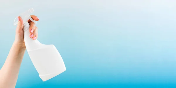 Woman hand sprays detergent from blank bottle on light blue background closeup