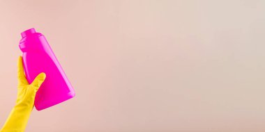 Koruyucu eldivenin içinde parlak pembe bir deterjan şişesi var.