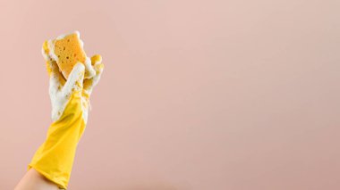 Kauçuk eldivenli kişi, bej kaplamasında köpüklü bulaşık süngeri taşır. Uzayı kopyala Pankart