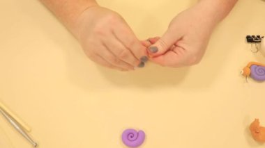 Bayan yoğurur ve yuvarlar turuncu polimer kilden elleri salyangoz için yuvarlak baş yapar