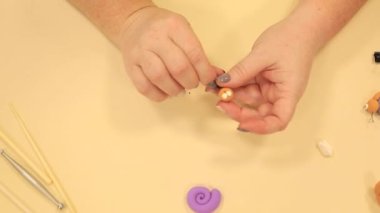 Kadın, polimer kil yüzünden yuvarlak salyangoz kafasının üzerine küçük siyah noktalar takıyor.